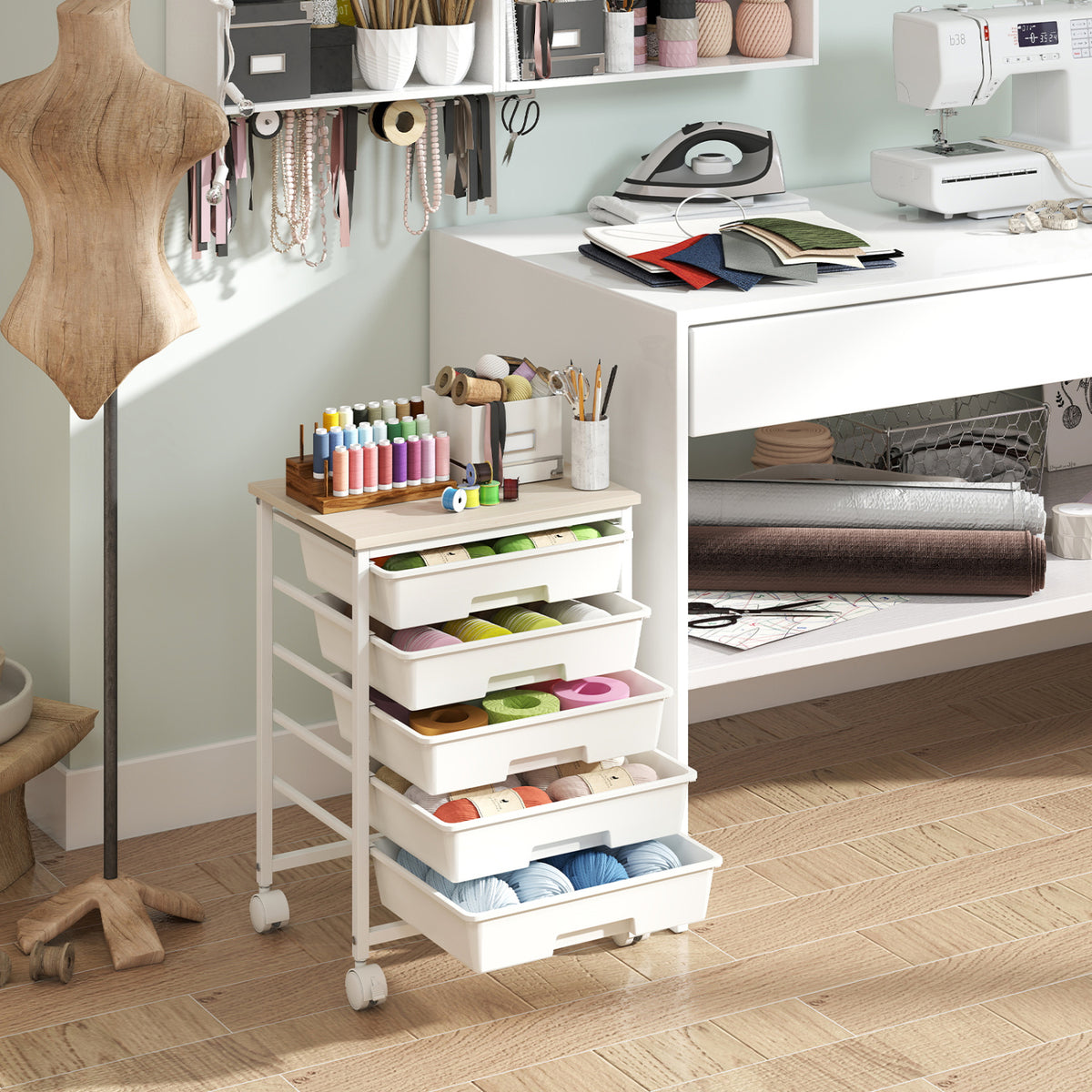 White five-drawer cart filled with sewing supplies in a craft room, with thread and tools on top.