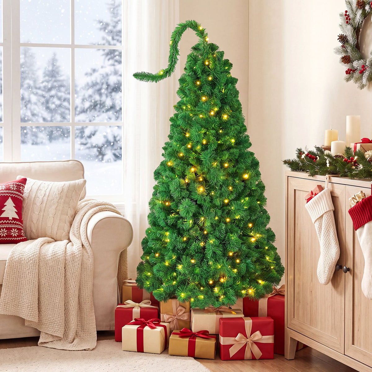 Green flocked tree with glowing lights and wrapped gifts beside a cream armchair and wooden cabinet.