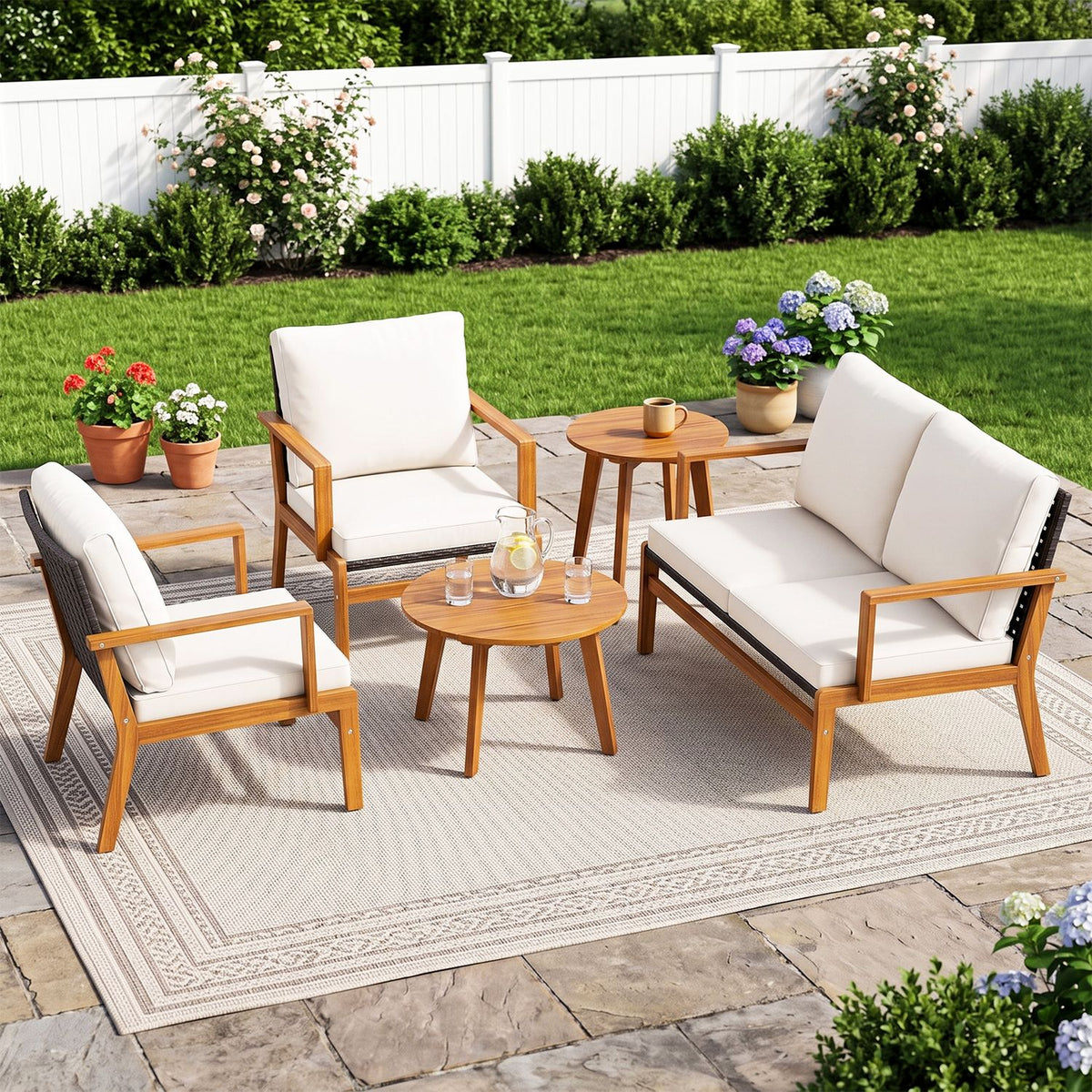 Cushioned patio seating and two round tables arranged on a rug in a garden setting.