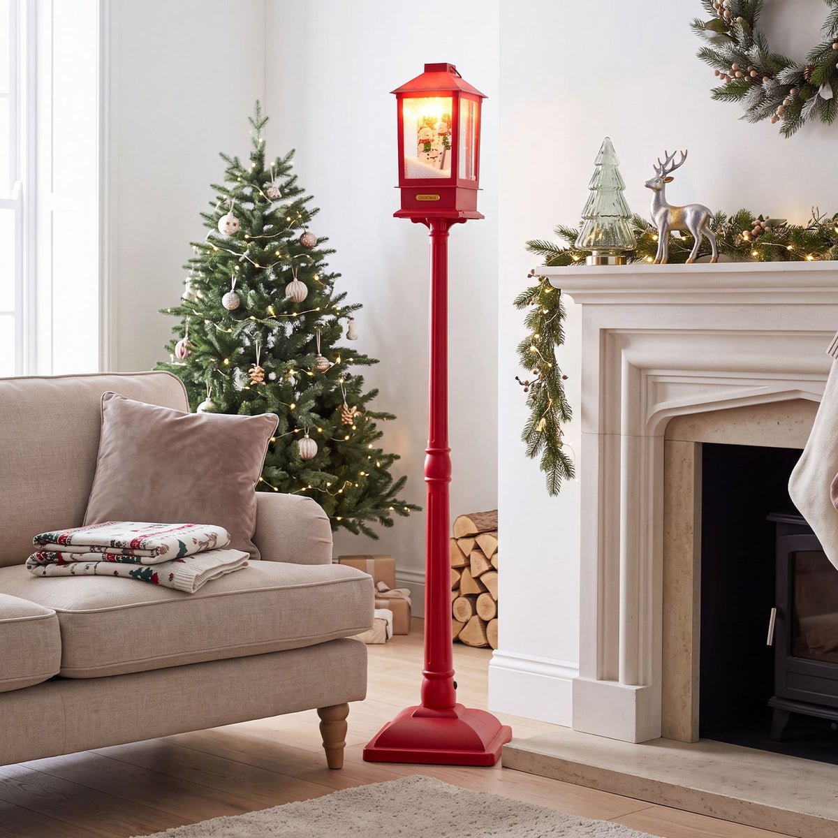 Red illuminated Christmas streetlight displayed between a decorated tree and a fireplace.