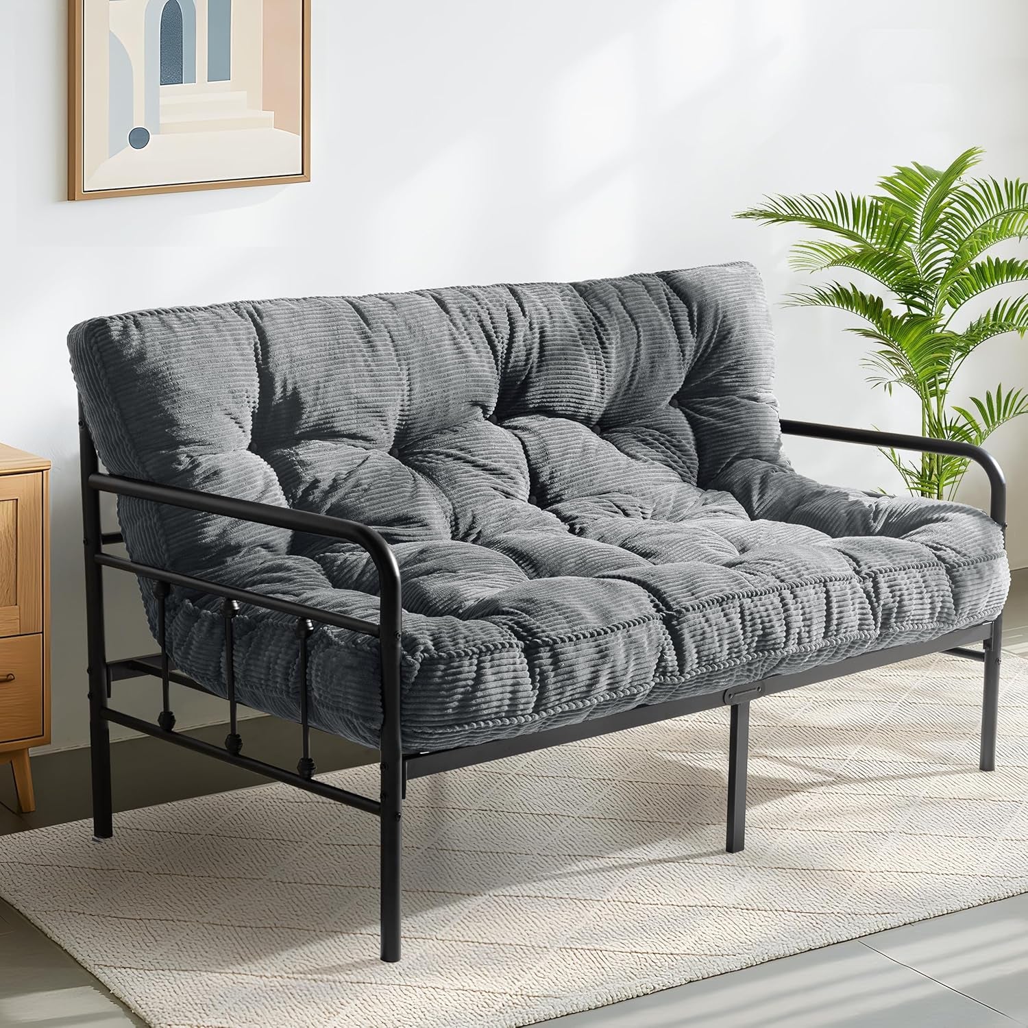 Three-quarter view of a charcoal-gray tufted futon mattress on a black metal frame in a bright room.