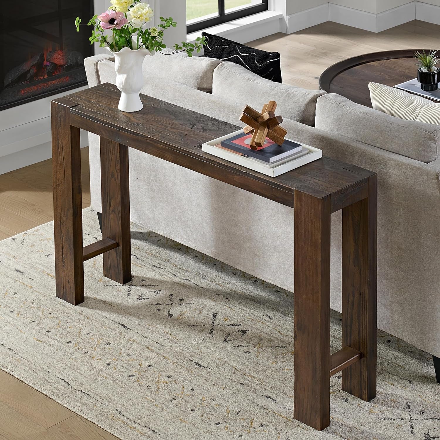Brown solid pine console table positioned behind a beige sofa with decorative objects on top