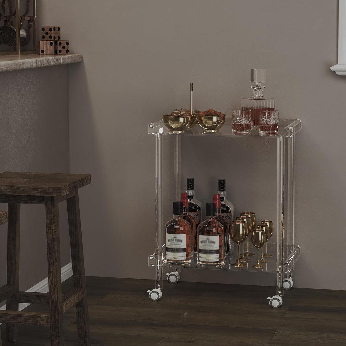Clear acrylic two-tier bar cart placed against a neutral wall beside a wooden bar stool on dark flooring