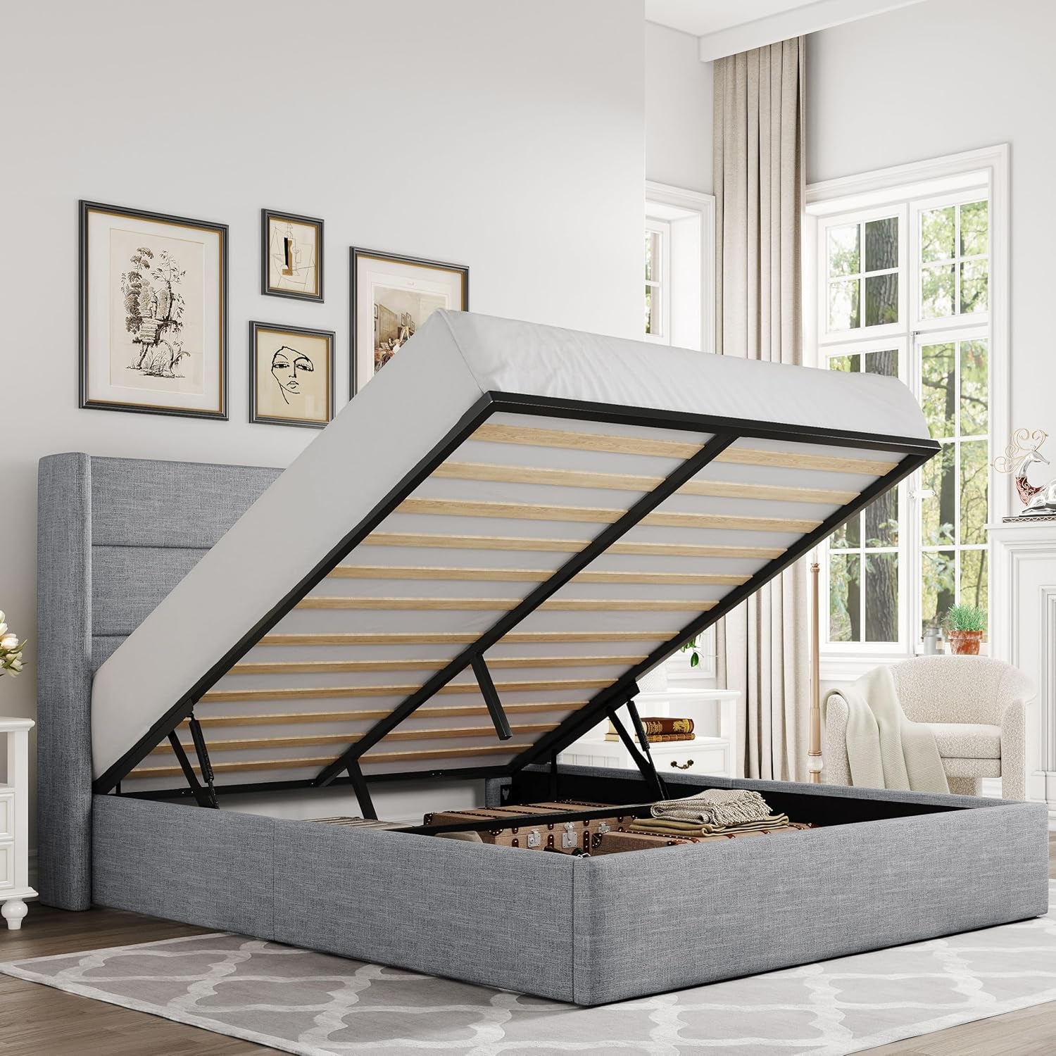 Gray upholstered wingback headboard bed with gas-lift mattress raised showing storage with suitcases inside