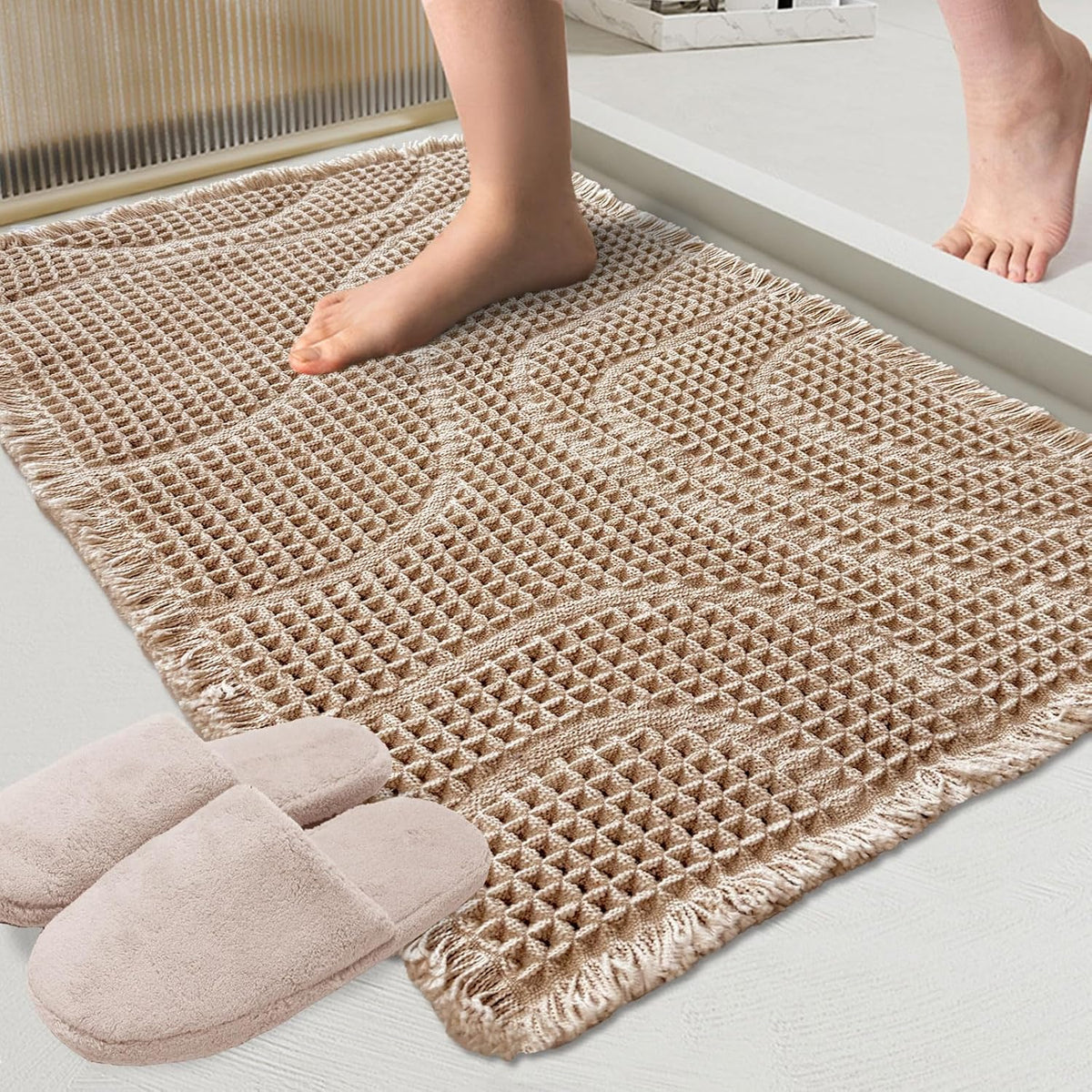 Beige textured rectangular bath mat with fringe and slippers at a tub step, foot stepping onto it