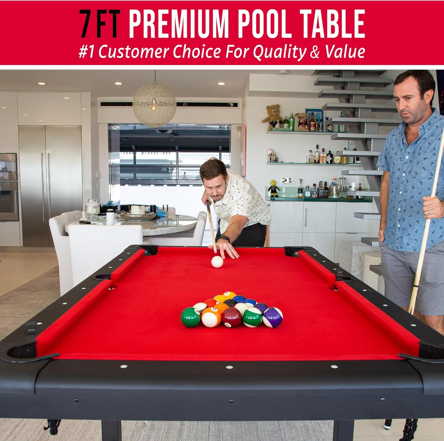 Red-felt billiards table in a modern dining/living room with two men playing a shot