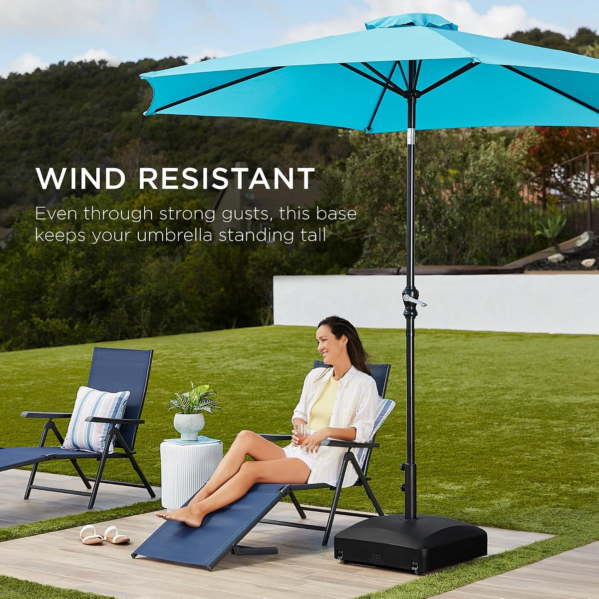 Black umbrella base on a patio with a turquoise open umbrella and lounge chair in a backyard setting
