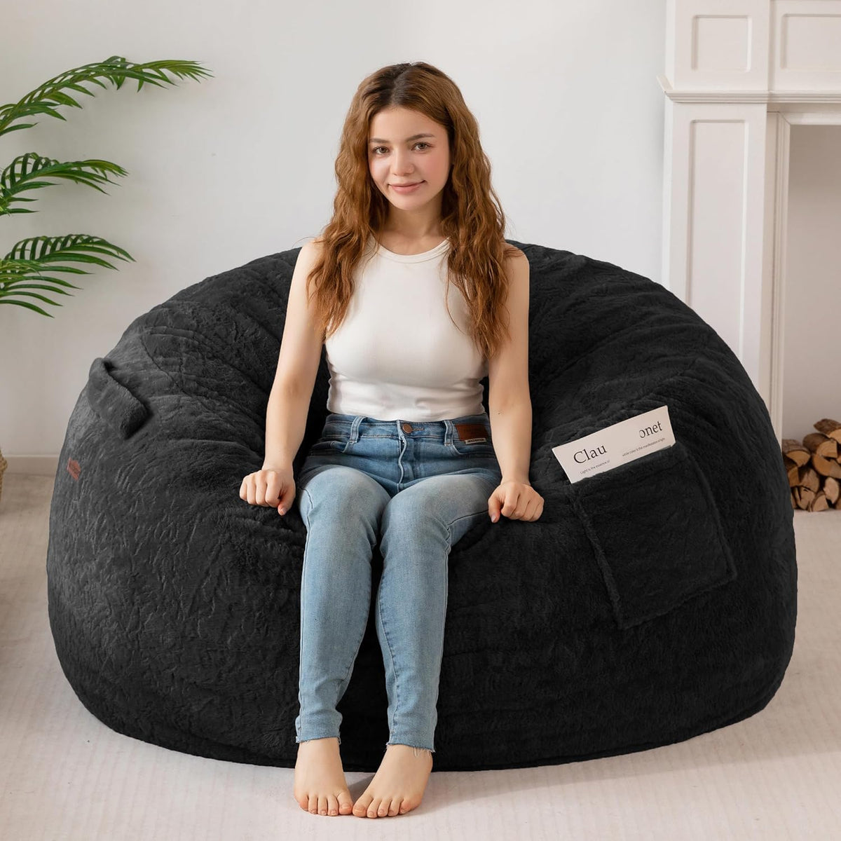 Front view of a charcoal black faux-fur bean bag with a seated model and a visible side pocket