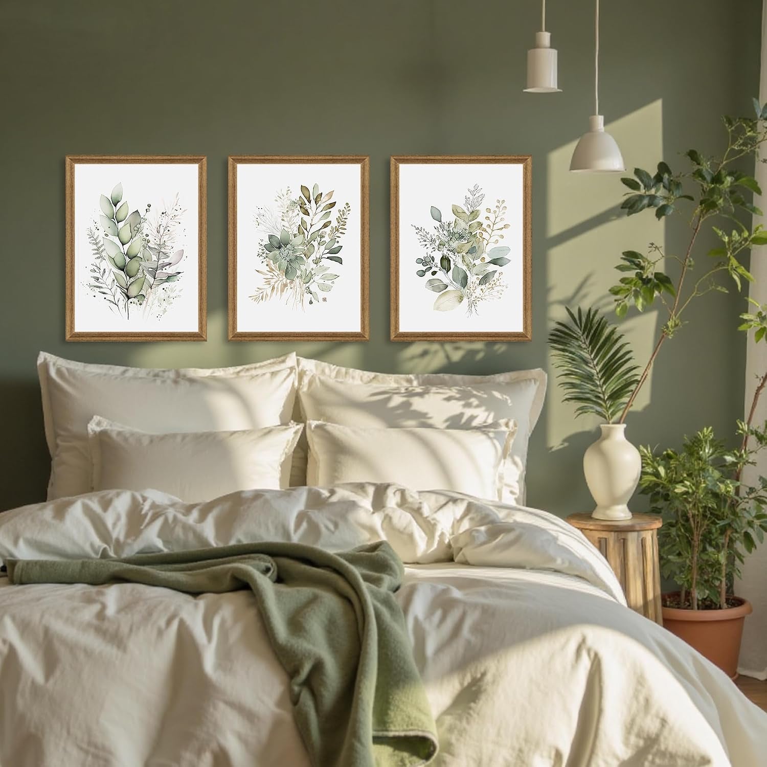 Bedroom scene showing three sage green botanical frames arranged above a bed against a green accent wall