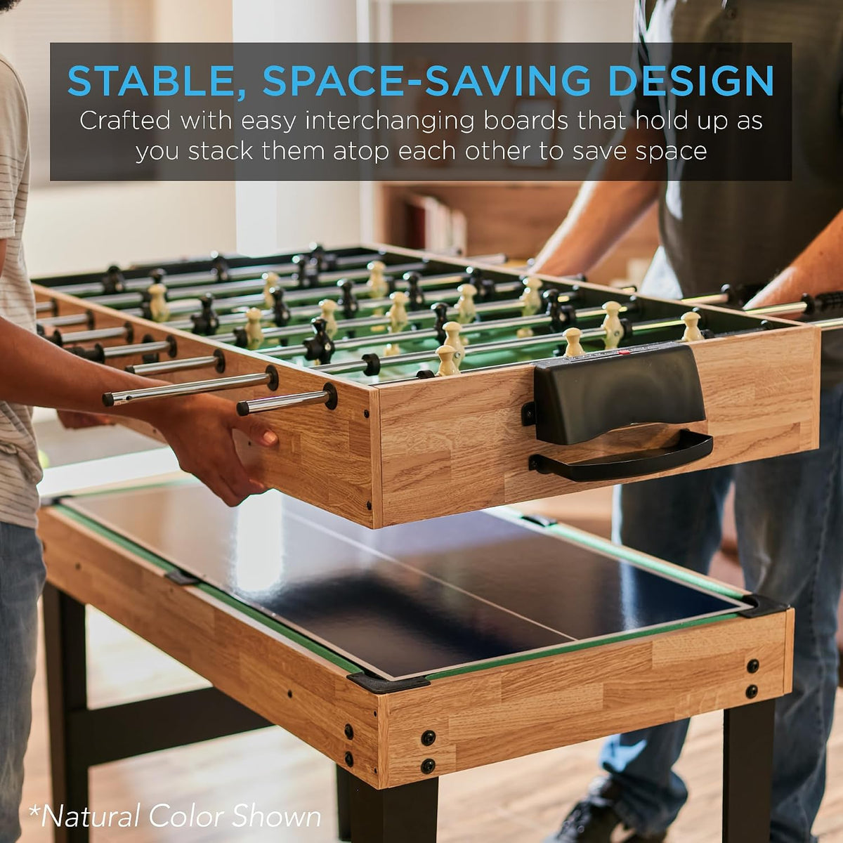 Two people lifting the foosball top to show interchangeable stacked boards over a table-tennis surface, natural finish