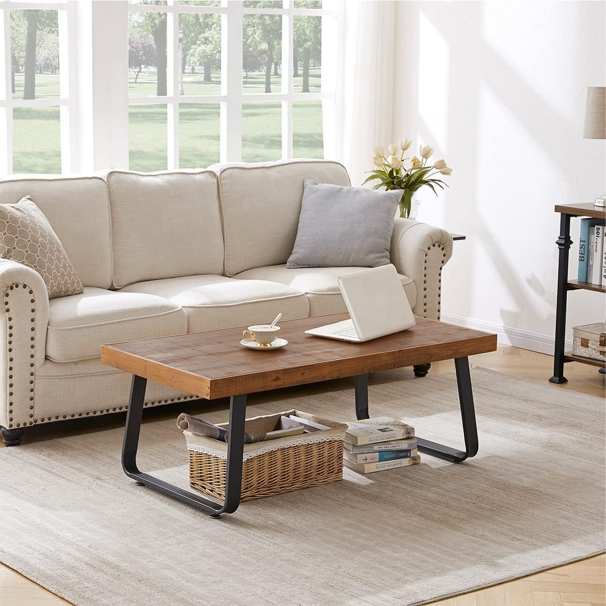 Rectangular wood coffee table with laptop and teacup, woven basket and books stored beneath in bright living room.