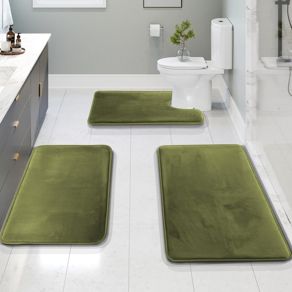 Bathroom view with three olive-green memory-foam mats placed along the floor, including a U-shaped mat at the toilet.
