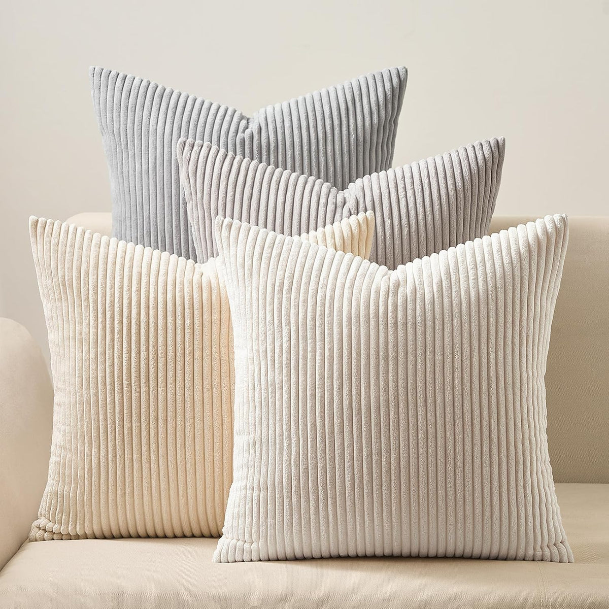 Four ribbed square pillows in soft neutral grays and creams on a beige sofa
