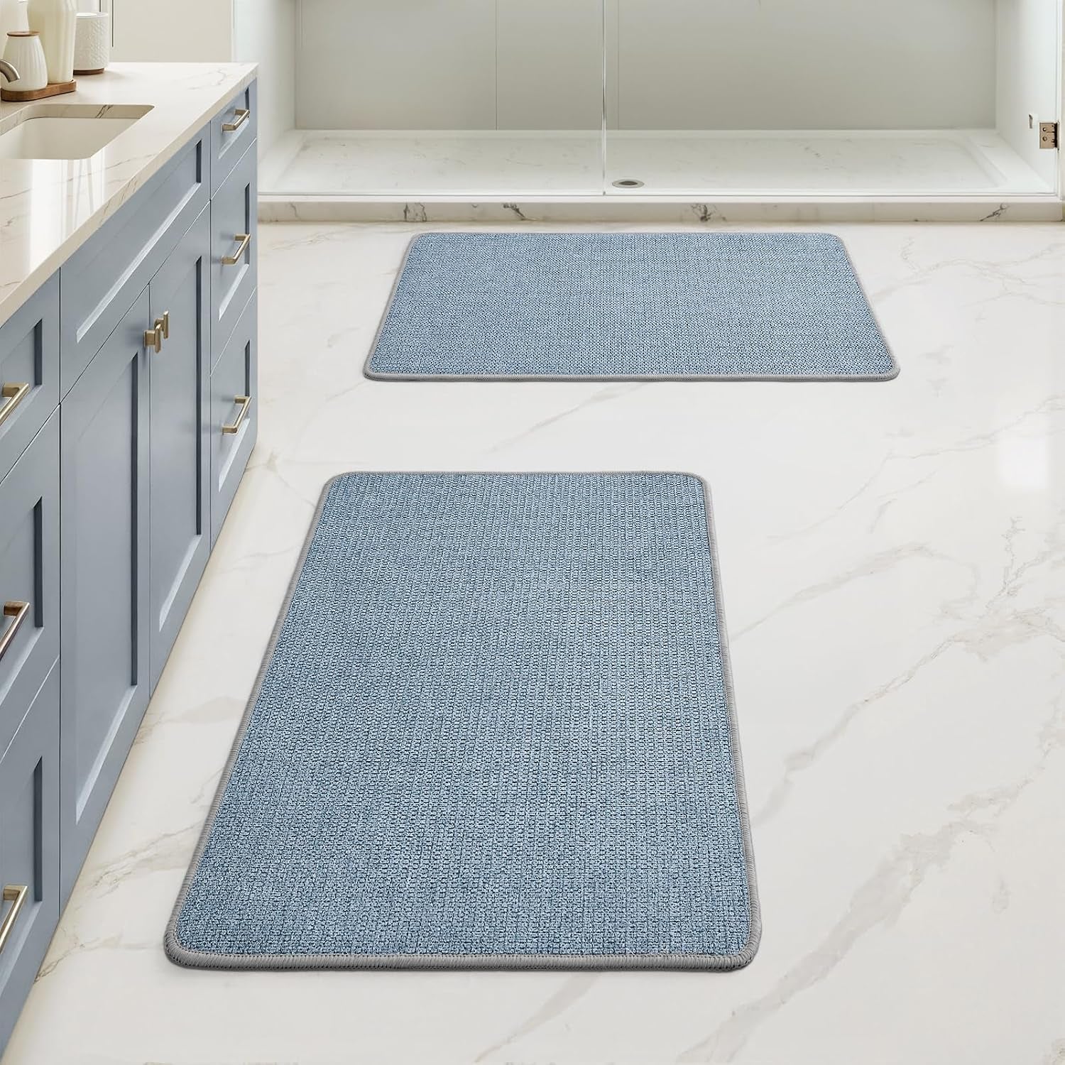 Bathroom floor with two rectangular blue bath rugs placed in front of a vanity and shower