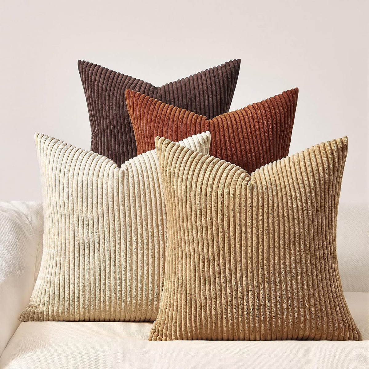 Four ribbed corduroy square pillows arranged in cream, tan, burnt orange and dark brown.