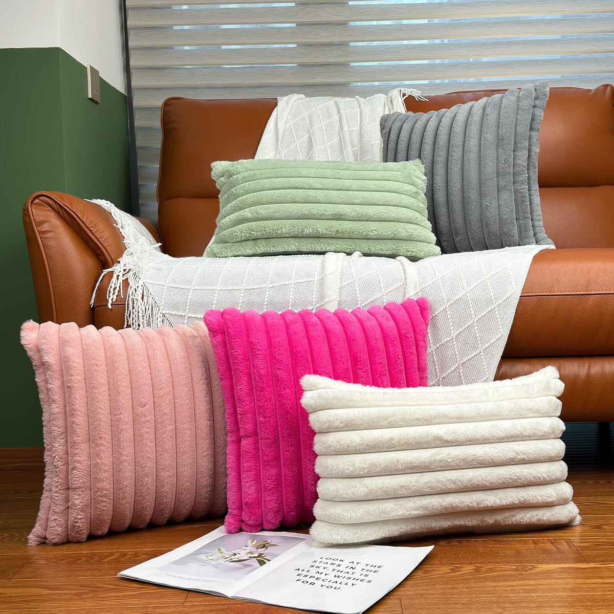 Assortment of ribbed faux-fur pillows in soft pink, hot pink, cream and sage displayed in front of a sofa.