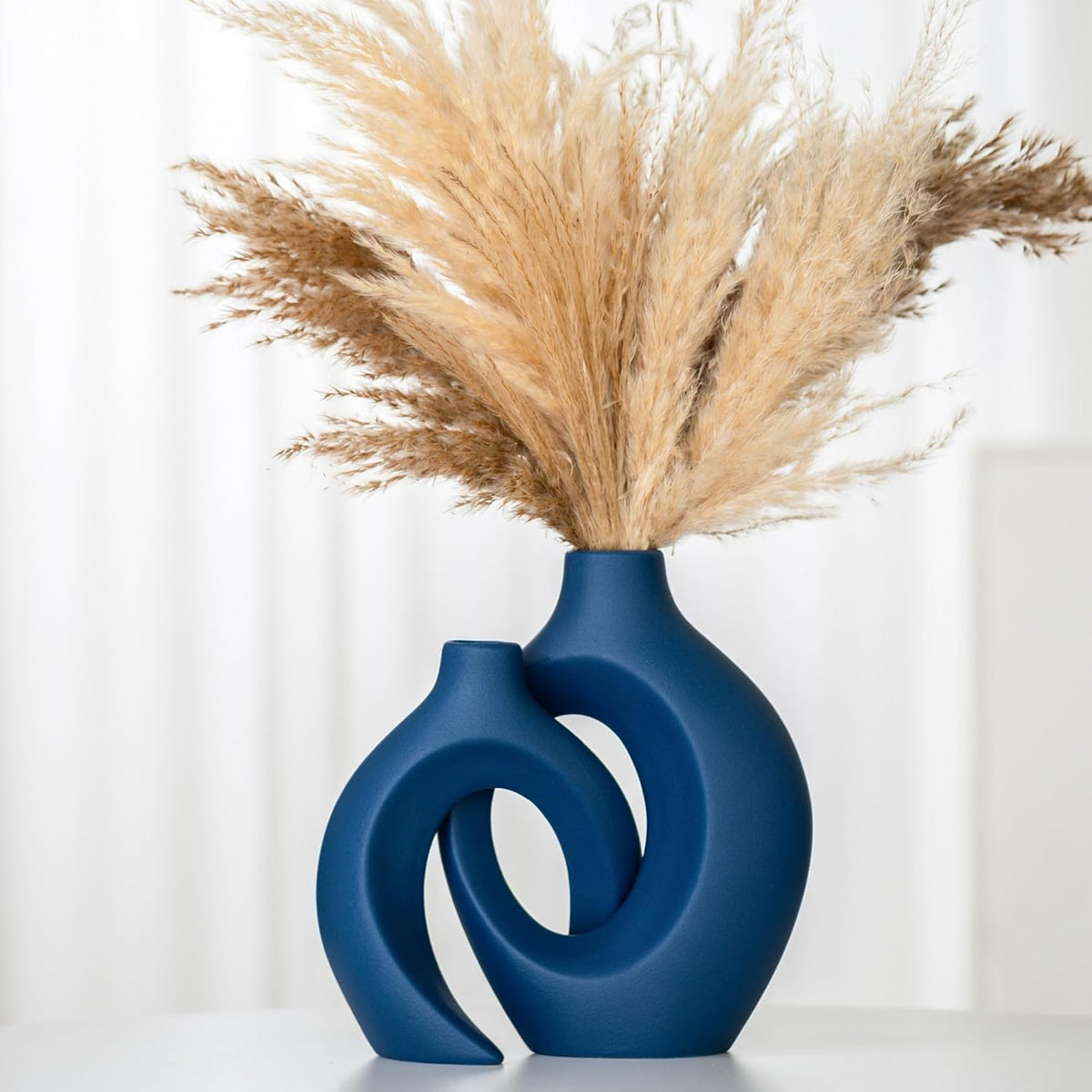 Close-up angled view of the blue vase set showing the intertwined openings and pampas grass flare.