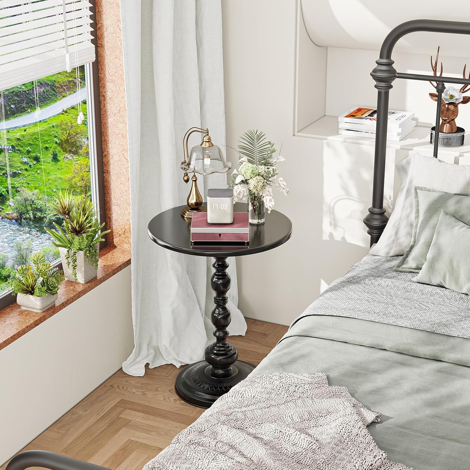Black round side table placed beside a bed styled as a nightstand in a bright bedroom