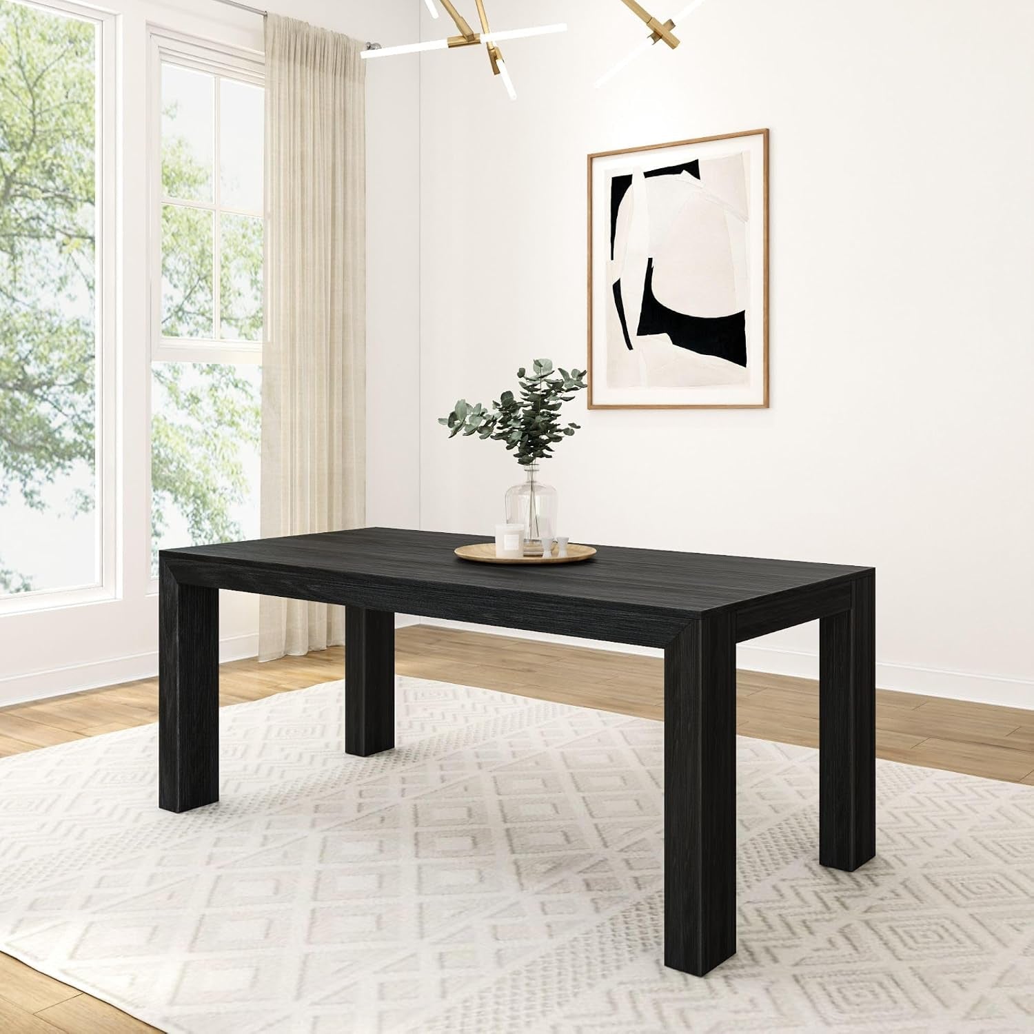 Rectangular black dining table on a light rug under a modern chandelier with small centerpiece.