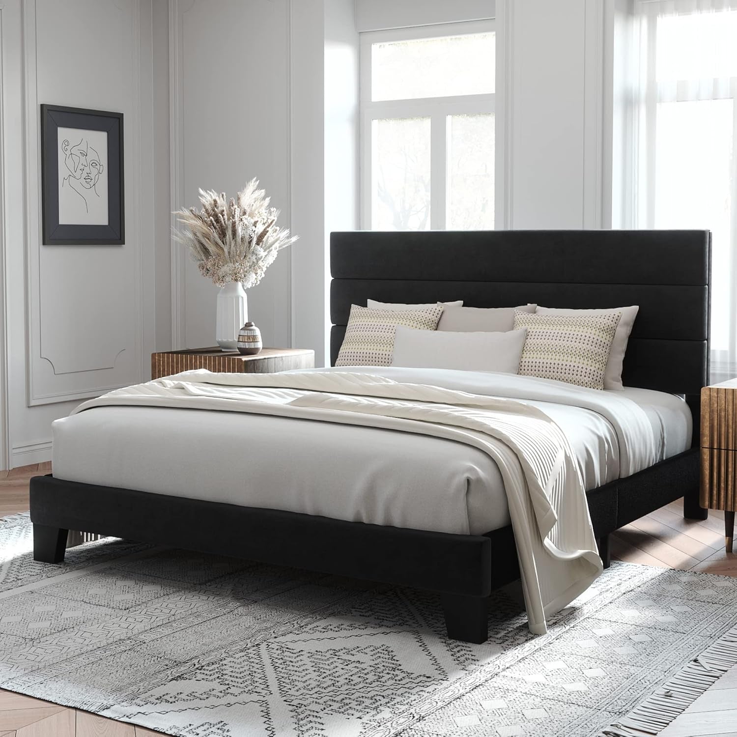 Angled bedroom view of a black upholstered bed with a three-panel headboard and white bedding.
