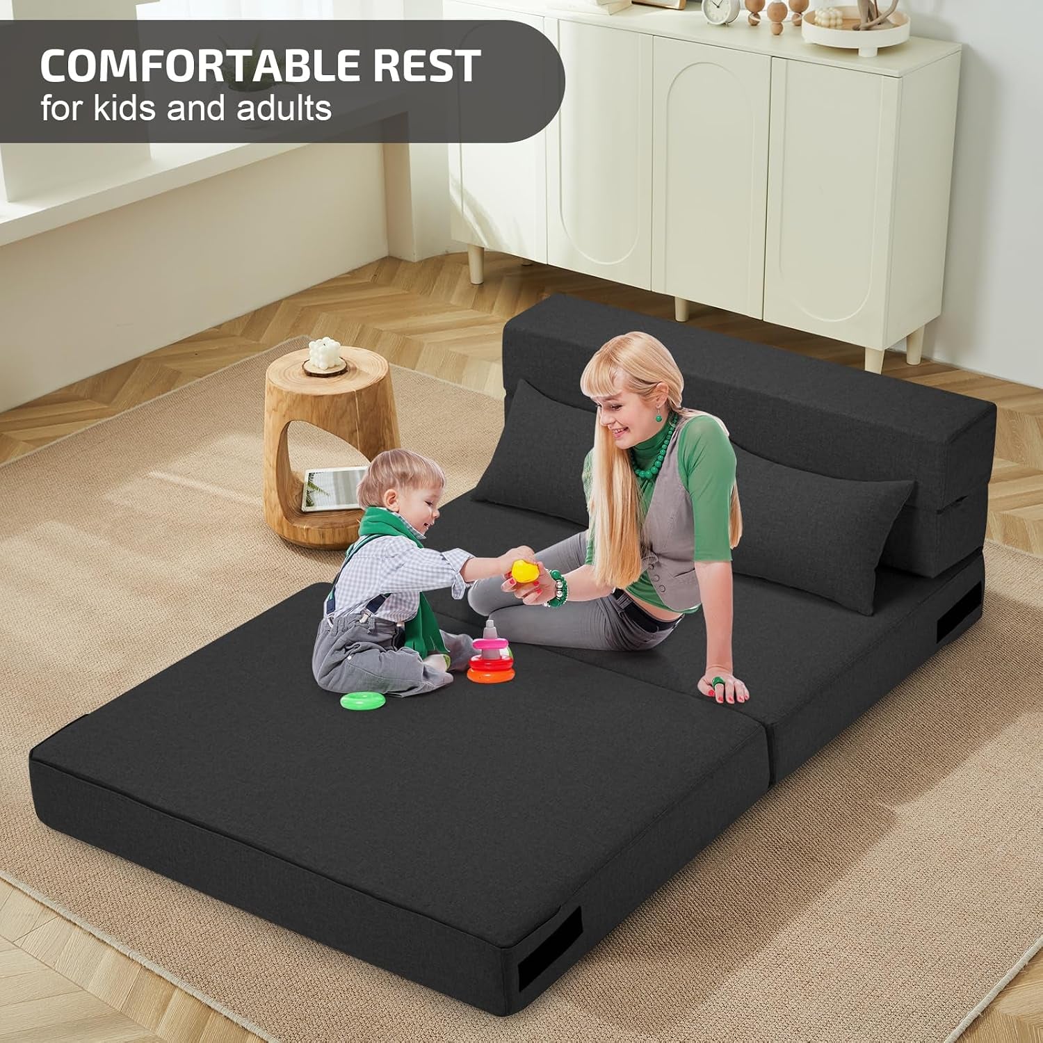 Dark gray sofa bed fully unfolded to mattress with woman and child sitting on it in a living room
