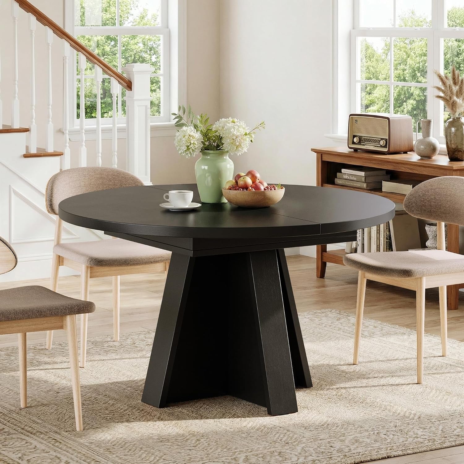 Black round dining table with pedestal base set in a bright dining room with four chairs.