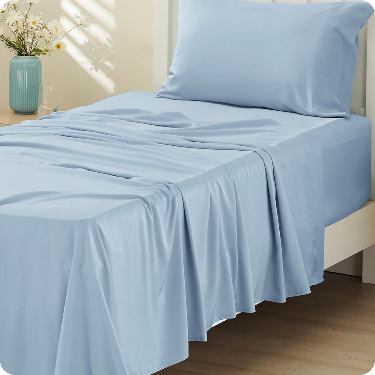 Close side view of a bed with light-blue sheets and pillow, the sheet draping over the mattress edge near a vase on a