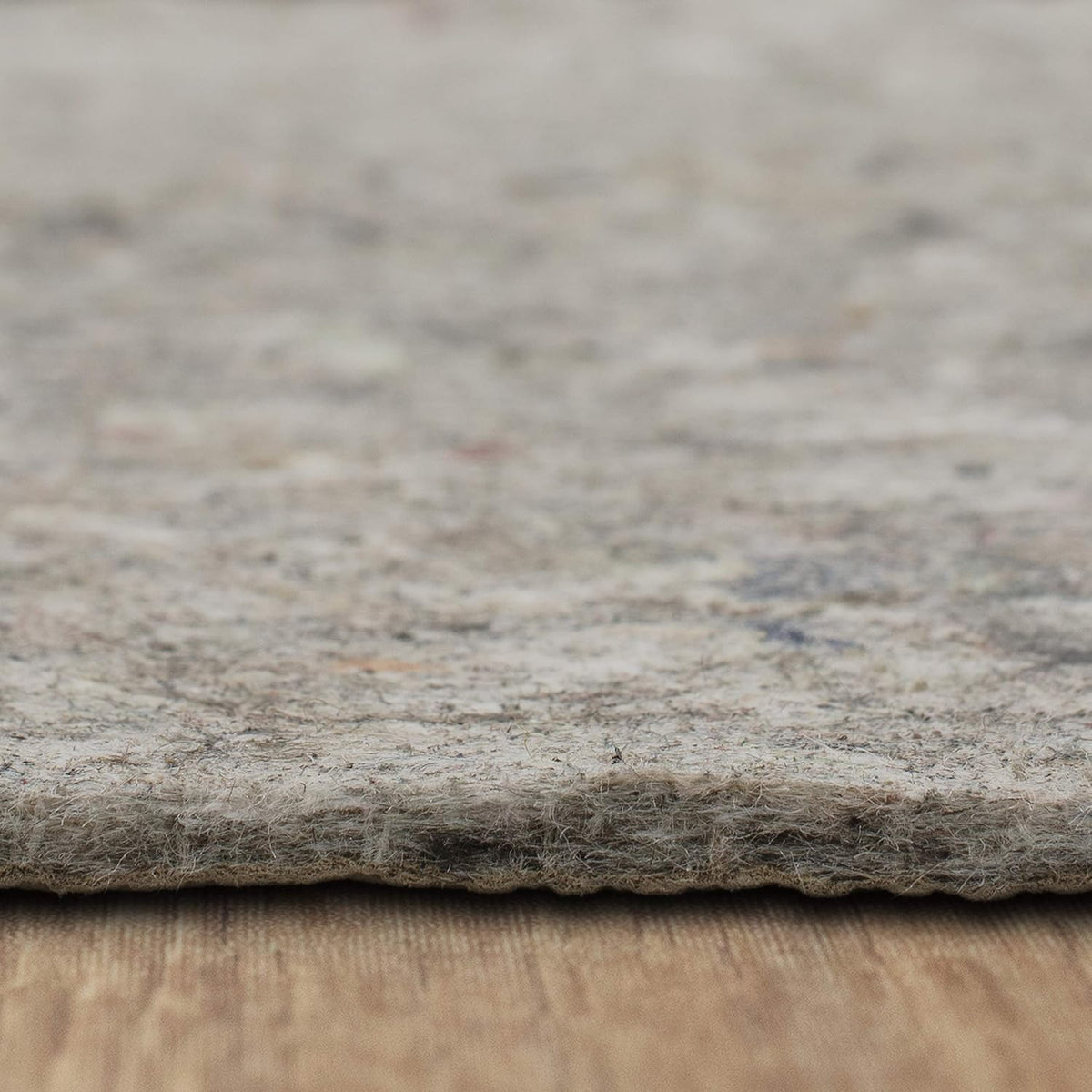 Tight side view of the pad edge on a textured floor, highlighting loose fibers and layered thickness.