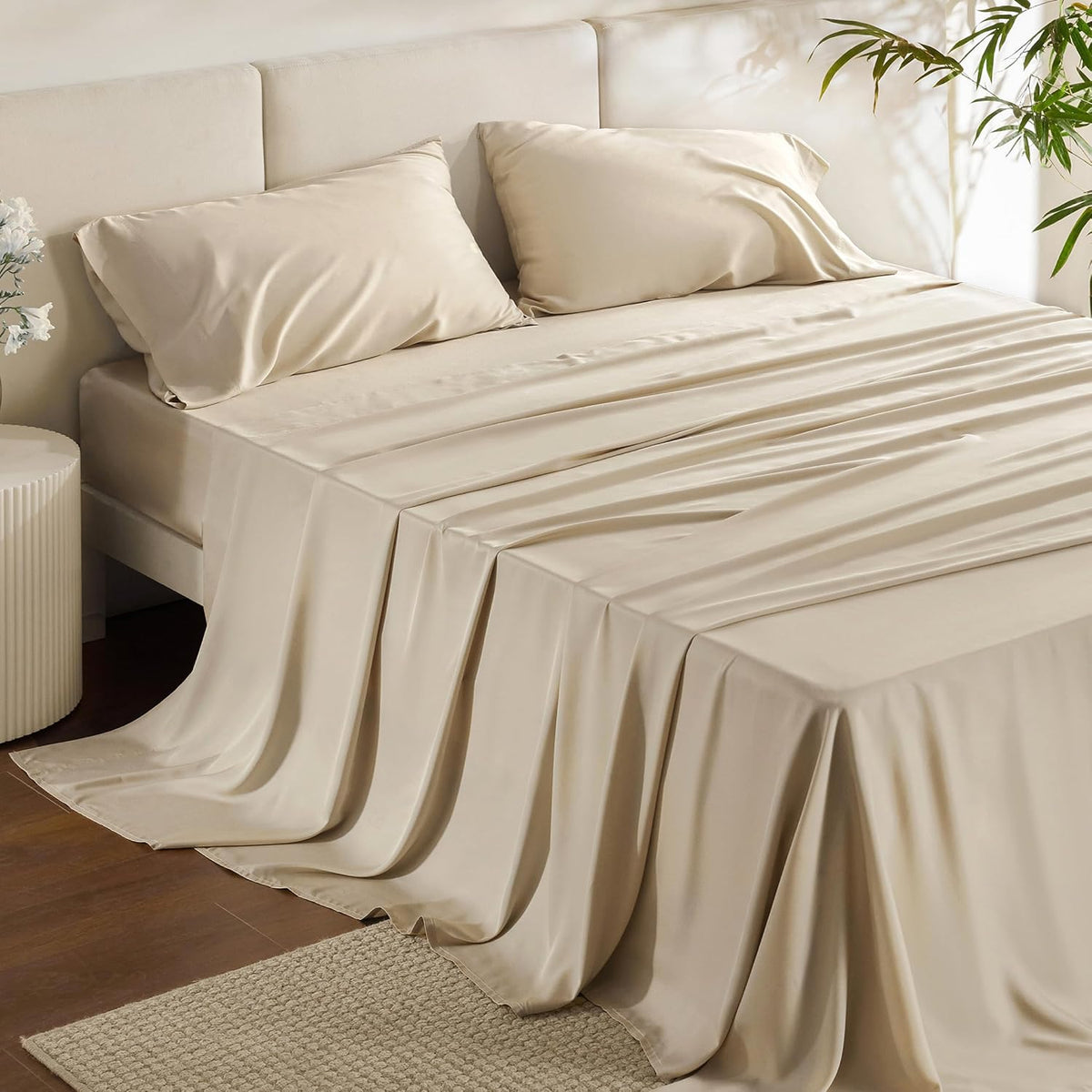 Angled detail of a bed with warm beige silky sheets flowing over the floor and two matching pillows.