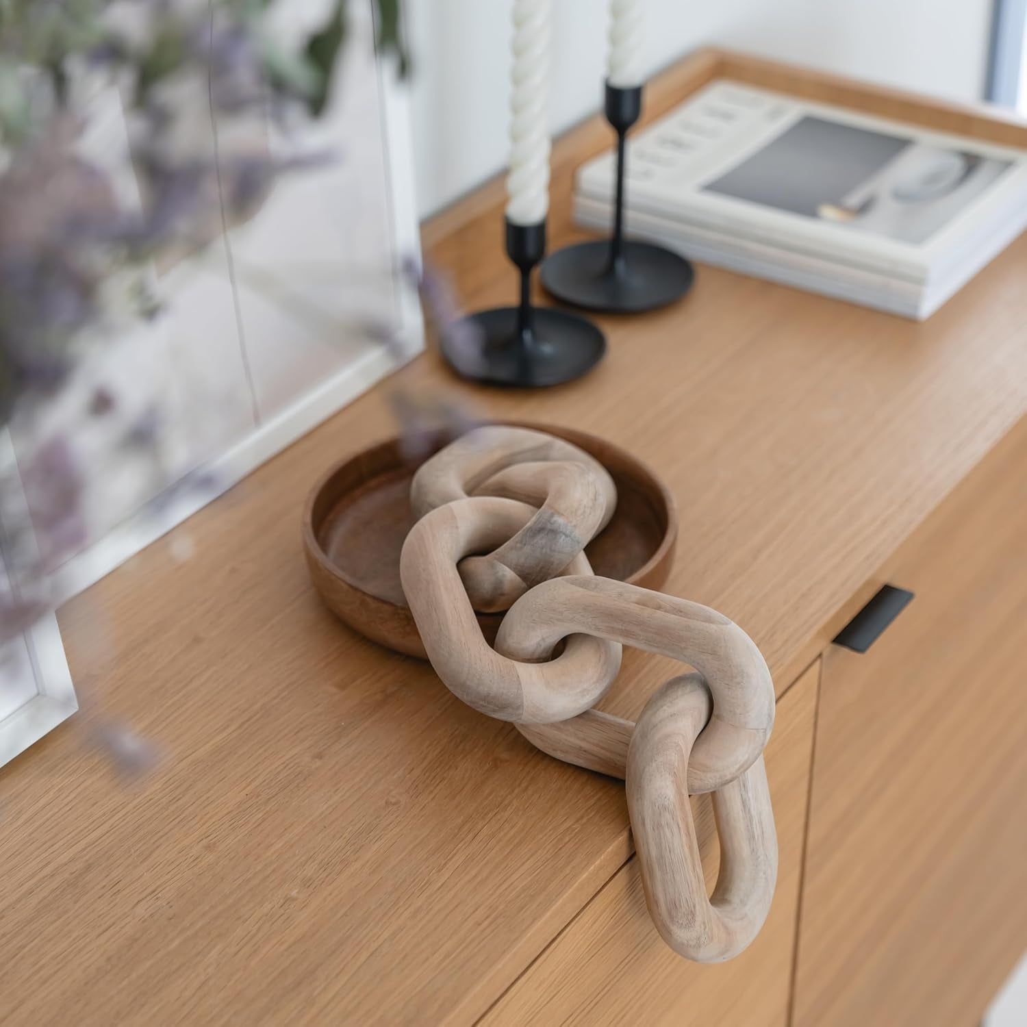 Matte-finish acacia wood chain placed partly inside a round wooden bowl on a light oak sideboard, top view.