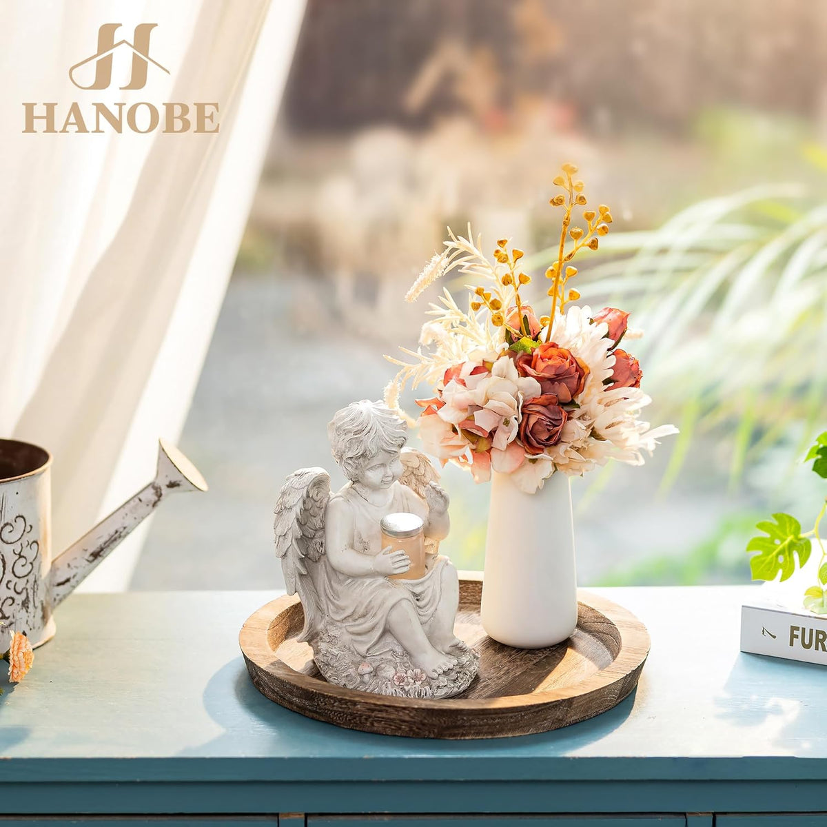 Wooden tray used as a base for a white vase of flowers and a small angel statue by a sunny window.