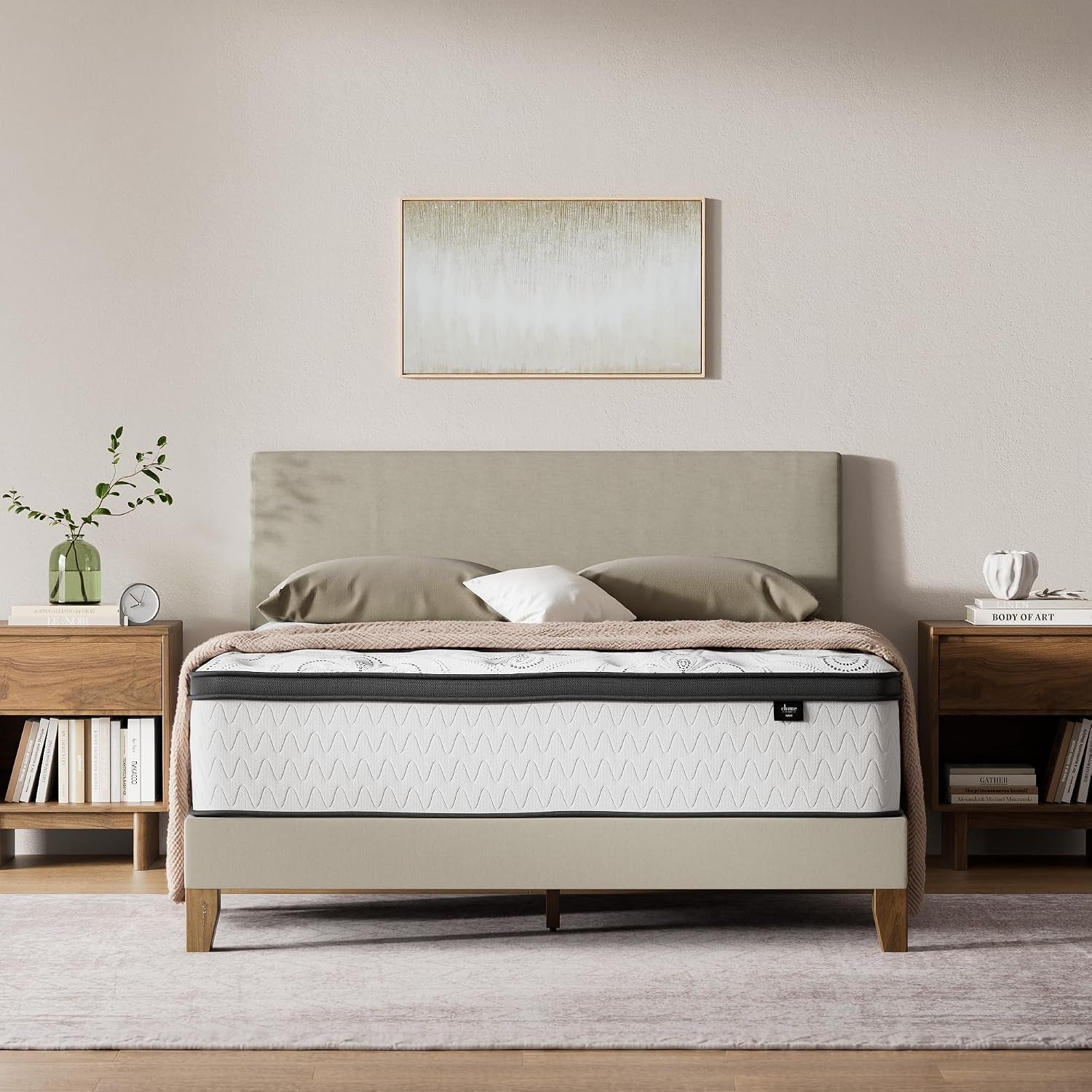Front view of a bed in a styled bedroom showing the mattress on a beige upholstered bed frame with nightstands.