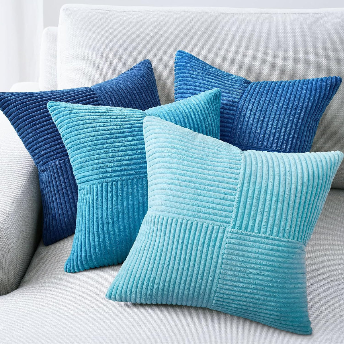 Four ribbed velvet pillow covers in shades of teal and aqua arranged on a light sofa corner.