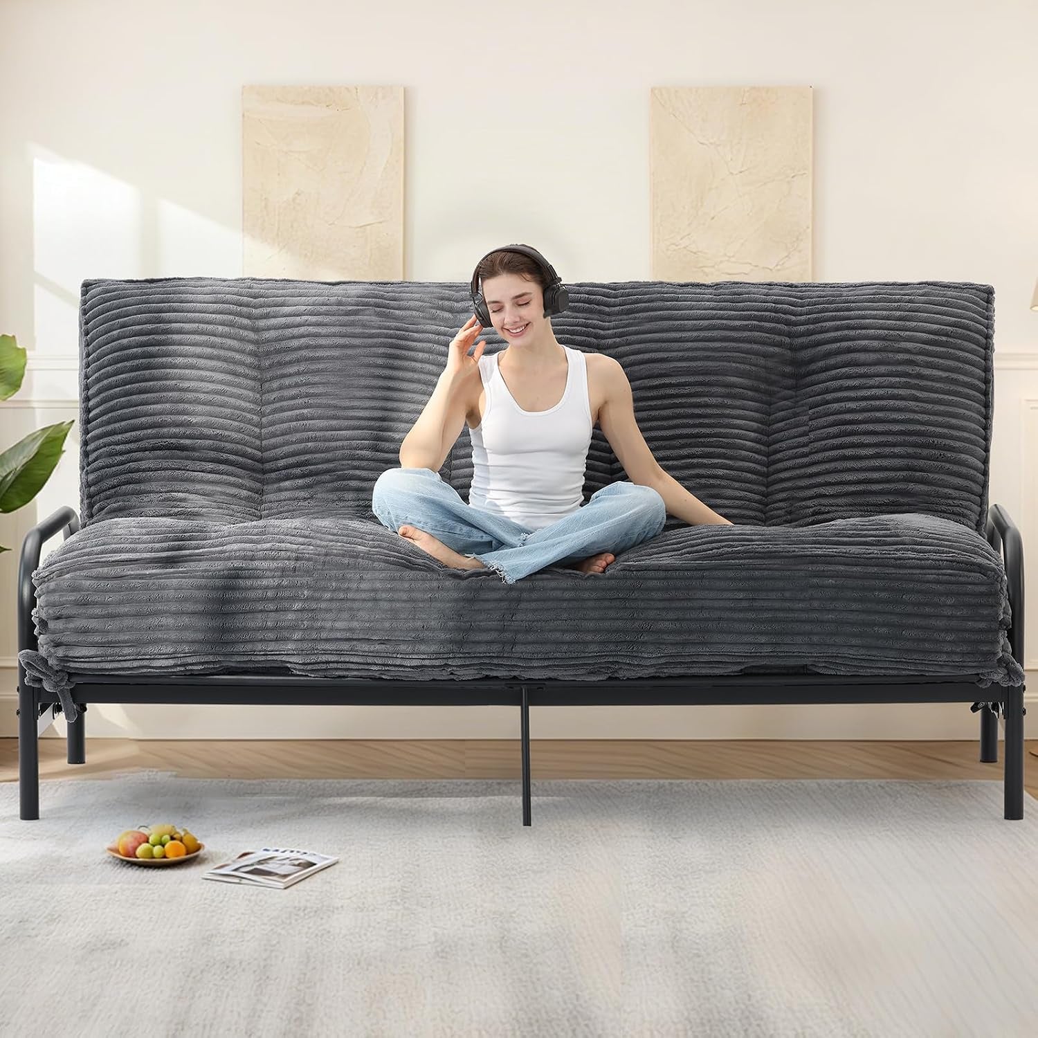 Front view of a dark gray ribbed faux-fur futon mattress folded into a sofa with a woman seated in the center, room decor