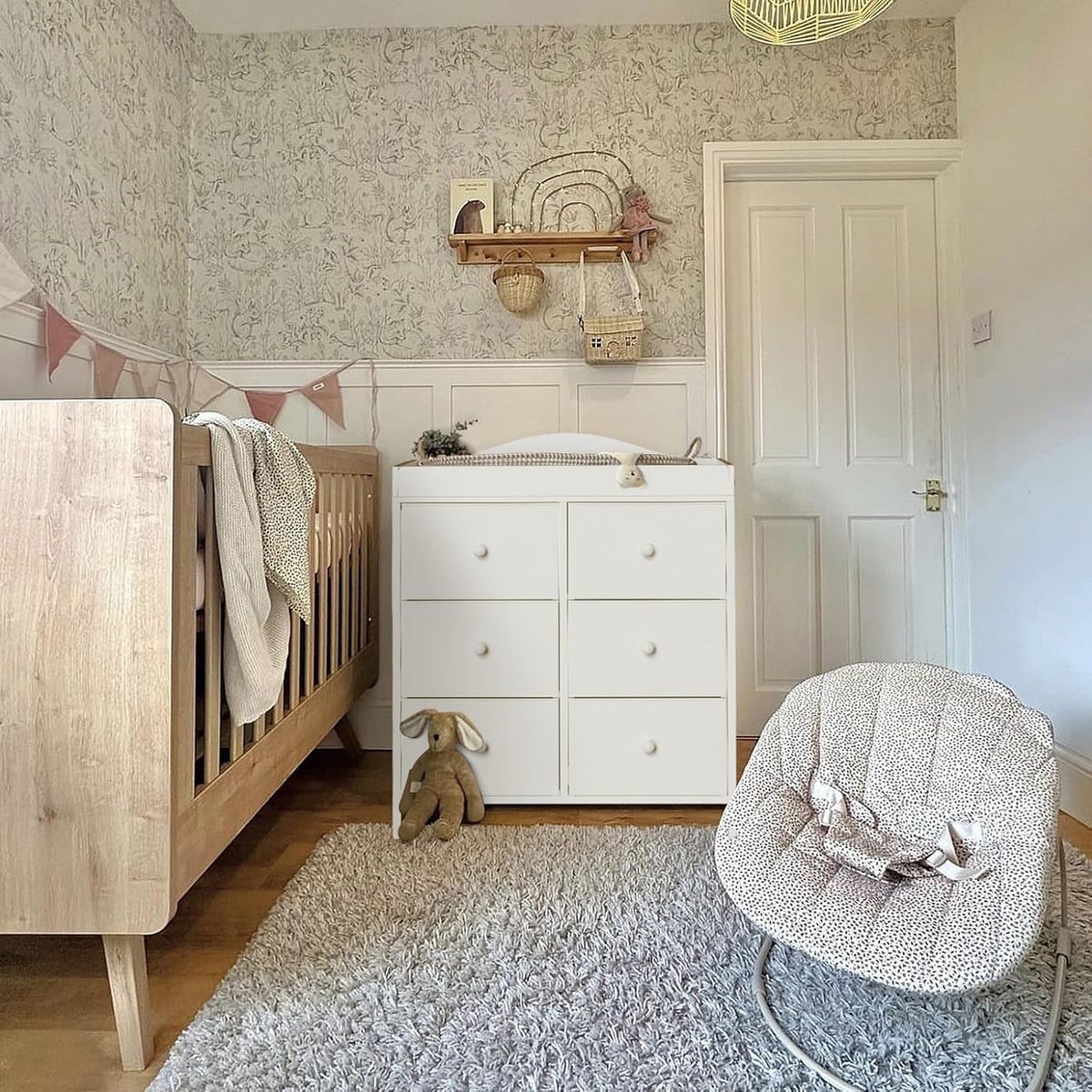 Nursery corner with a white six-drawer changing dresser between a crib and a baby rocker.