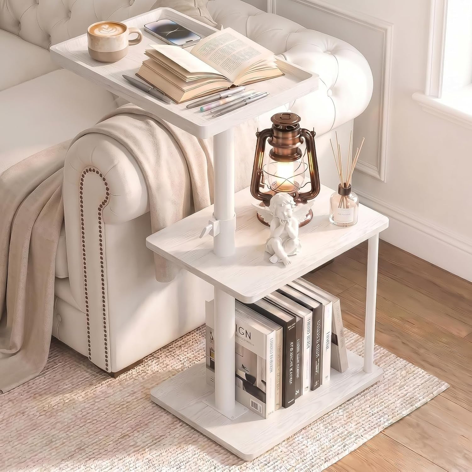 Same three-tier C-shaped table in white styled with books, a lantern and a mug next to a tufted sofa.