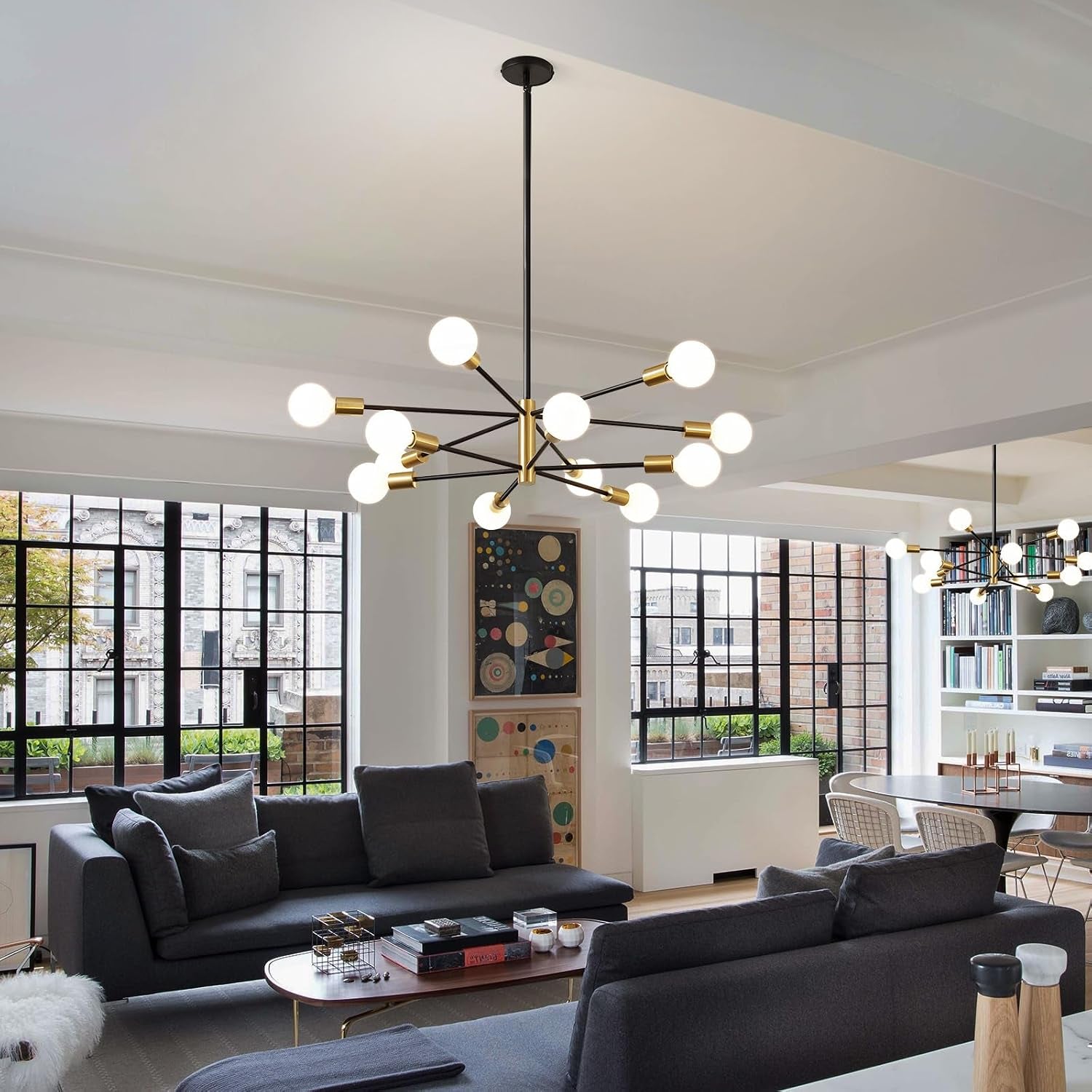 Chandelier centered in a bright living room with large industrial-style windows and gray sofas.