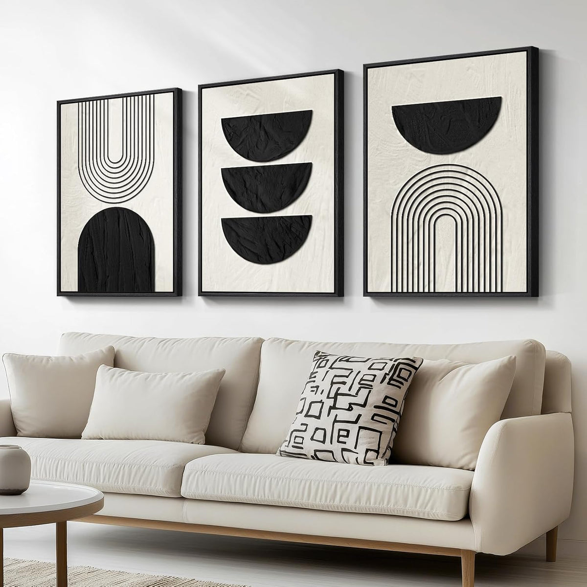 Three framed abstract panels with black shapes on textured cream background above a beige sofa.