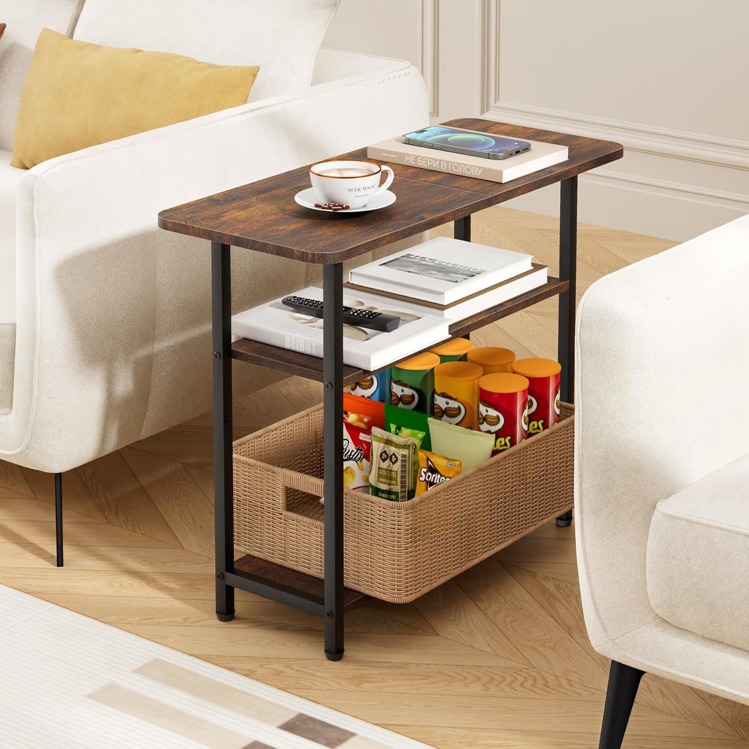 Brown three-tier side table placed between two sofas holding a cup, book and a woven basket on lower shelf.