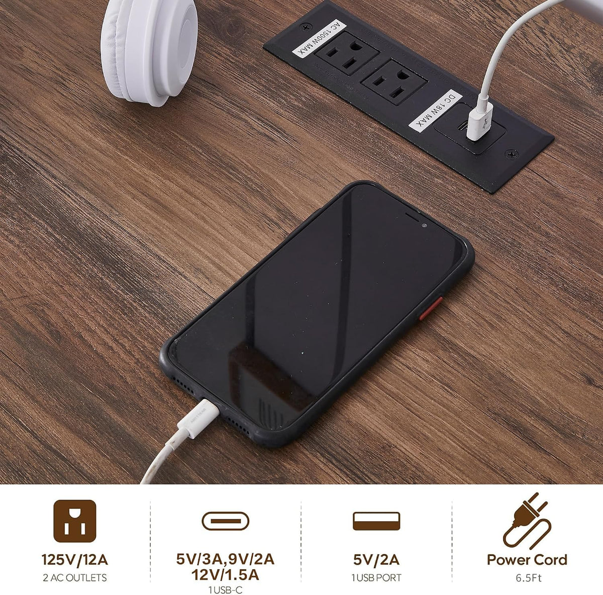 Close-up of wood-tone desk surface showing integrated charging station with AC outlets, USB and USB‑C port and a phone being‑