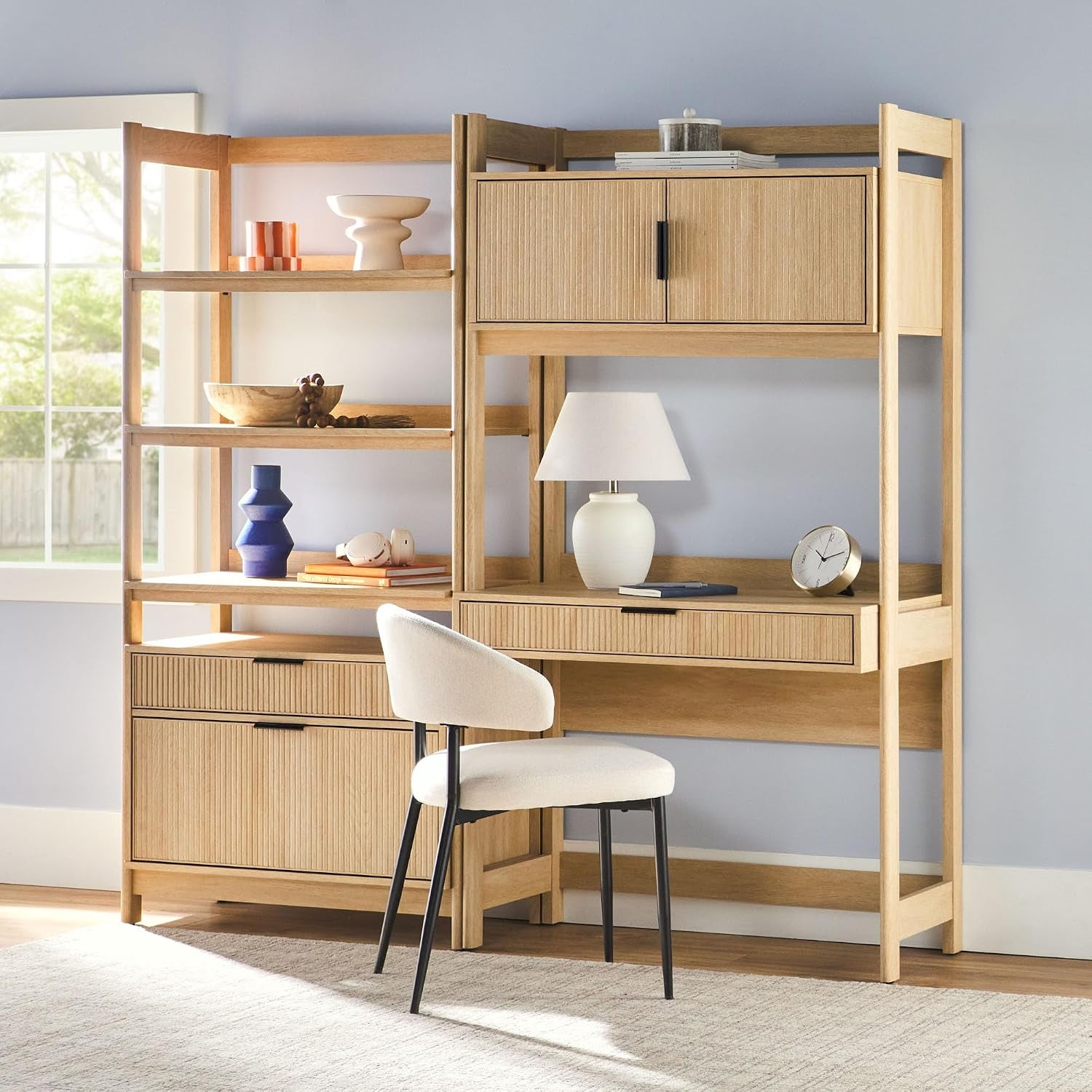 Light wood hutch desk and bookcase styled in a home office with a chair, lamp, clock, and decorative accessories on shelves.