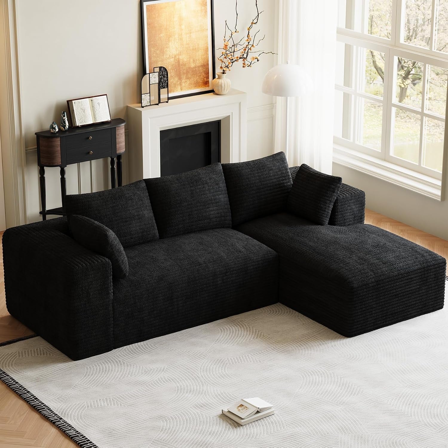 Black L-shaped modular sofa with chaise positioned by a fireplace and large window.