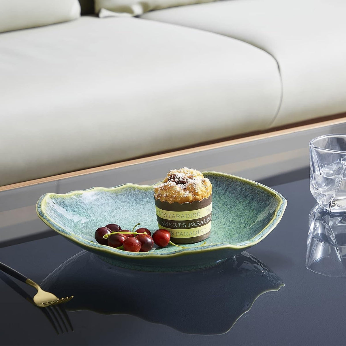 Shallow emerald bowl used as a serving dish with cherries and a muffin on a glass table, angled view