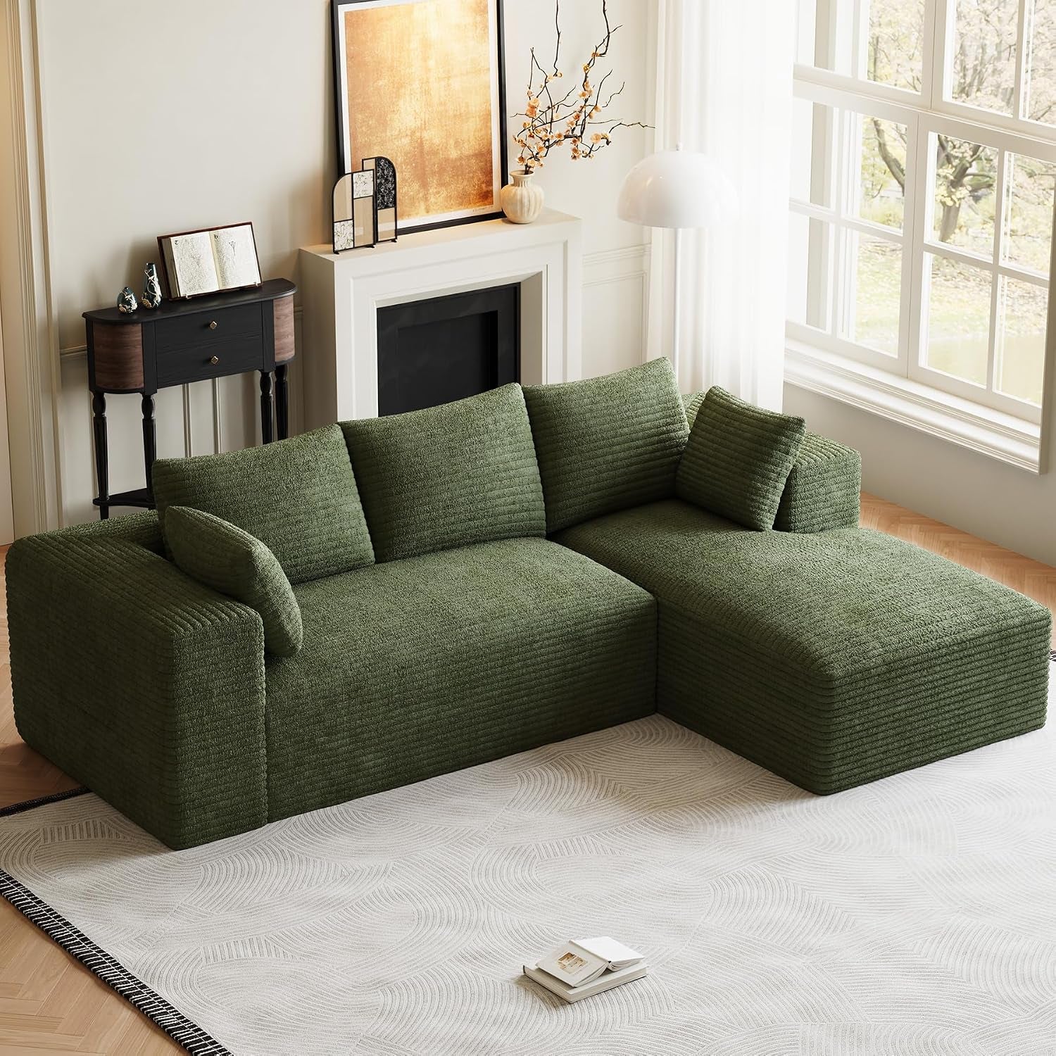 Angled view of olive green L-shaped modular sofa with chaise placed on a patterned rug near a fireplace.