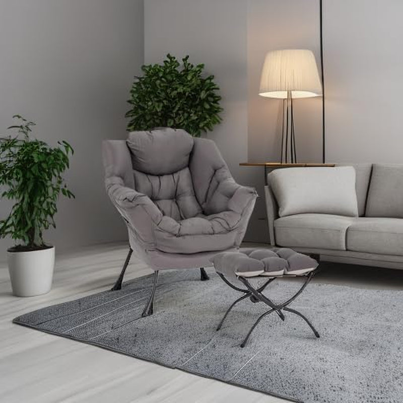 Grey padded lounge chair with matching ottoman on a rug beside a sofa, lamp and potted plants.