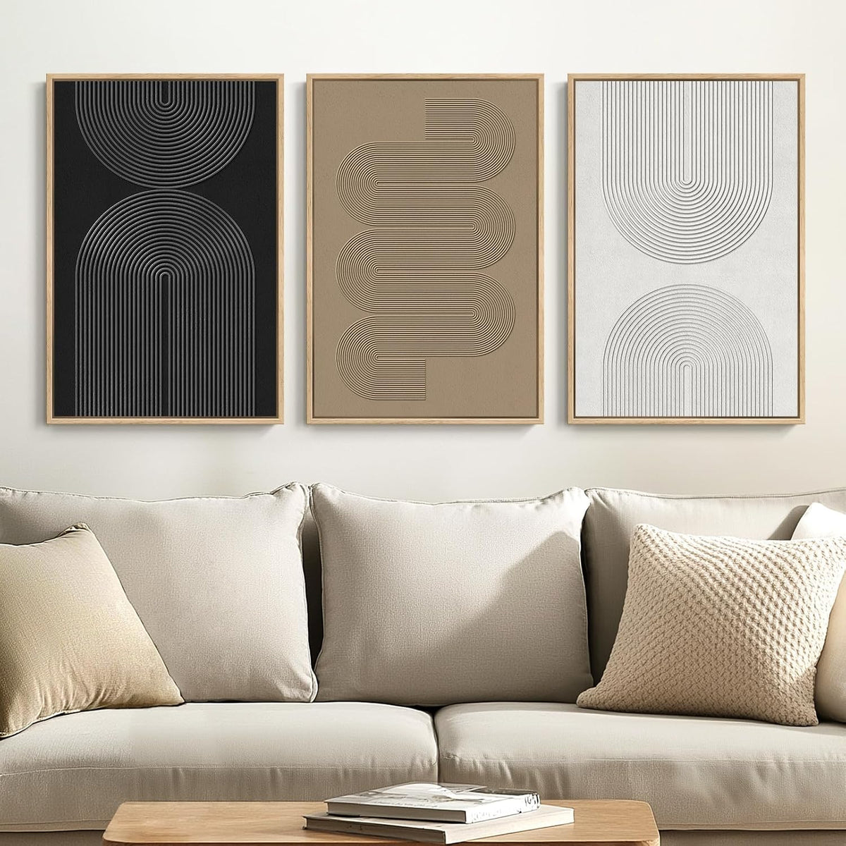 Triptych of geometric framed prints in black, tan and white displayed above a neutral sofa with pillows.