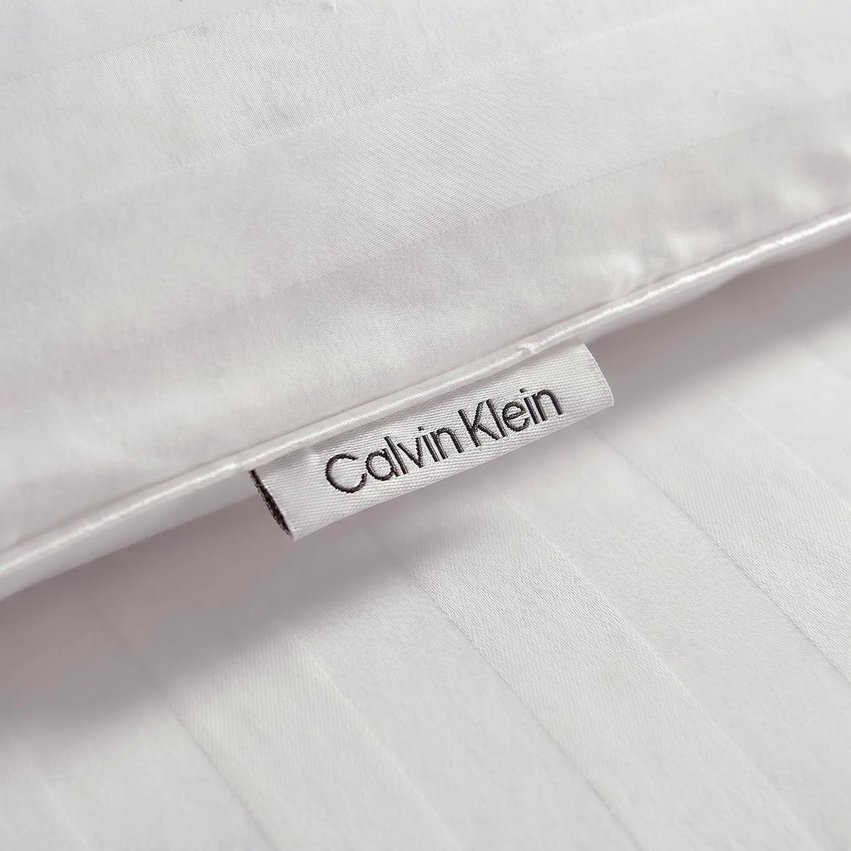 Close-up of a sewn fabric tag peeking from the edge of a white striped comforter cover