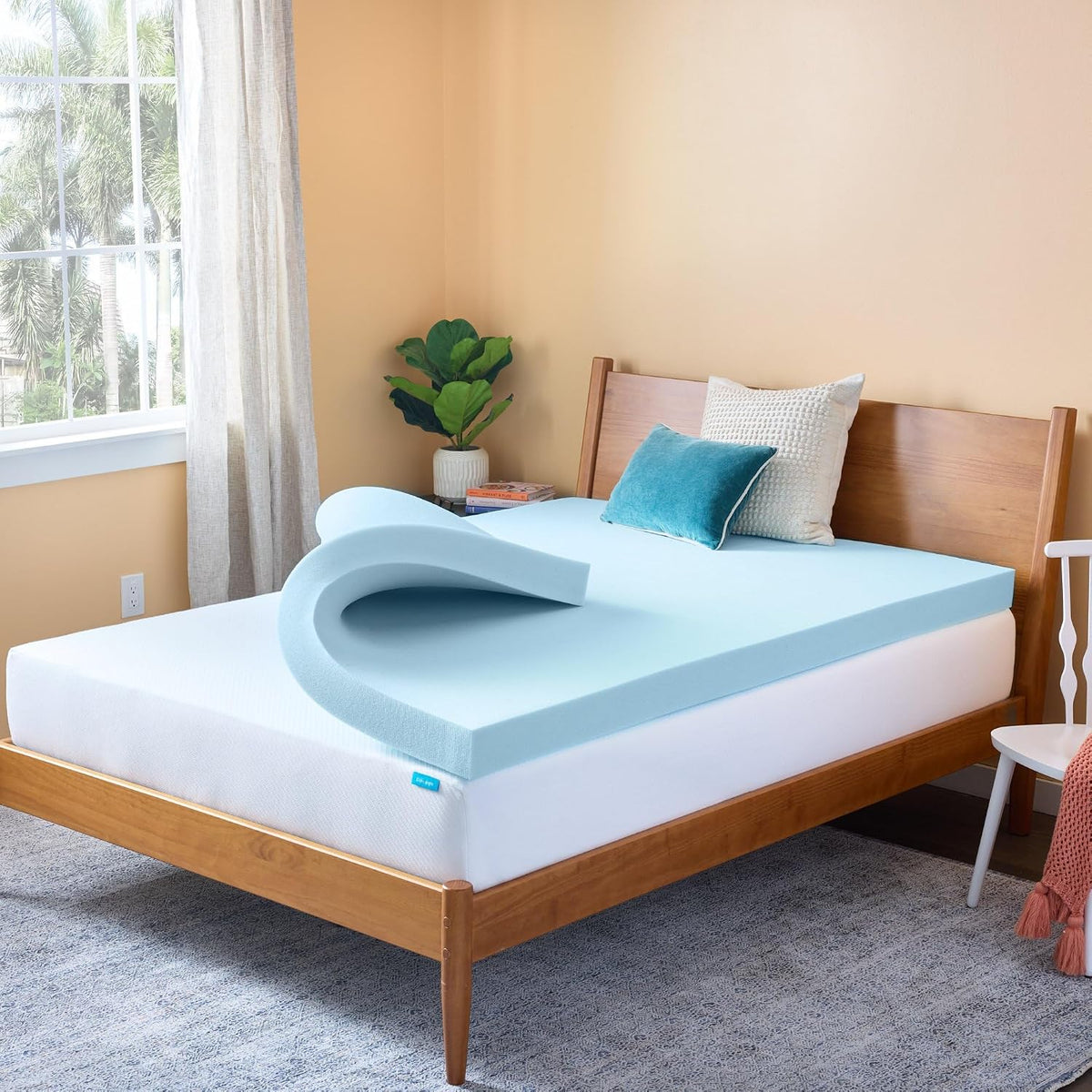 Angled bedroom shot of a light blue foam topper folded near the center of a bed with pillows