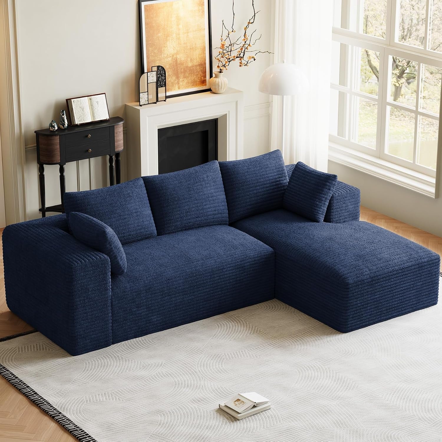 Three-quarter view of a navy blue L-shaped modular sectional with chaise under a bright window.
