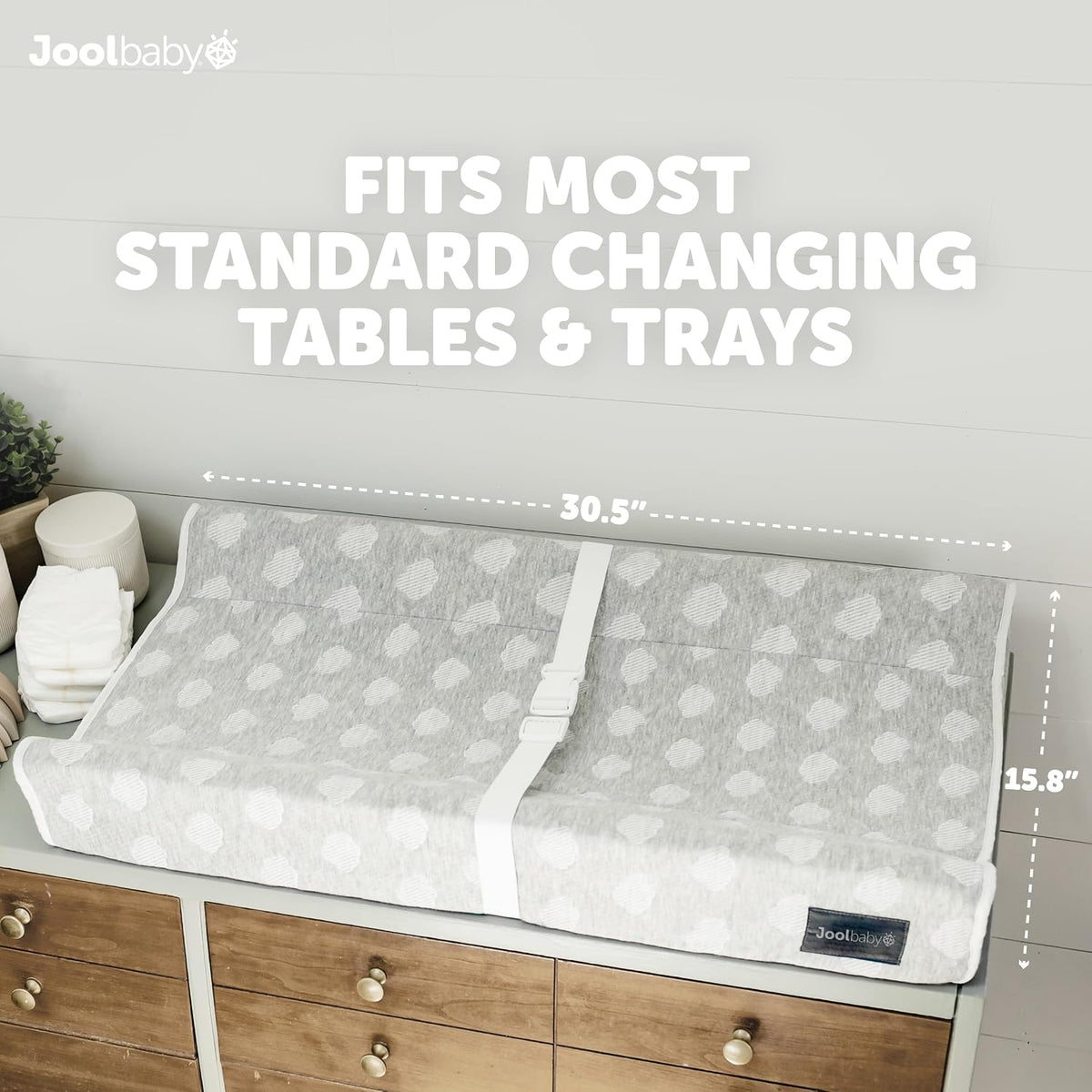 Top-down view of the gray contoured changing pad with heart pattern and central safety strap placed on a wooden dresser with
